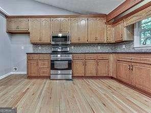 kitchen with lofted ceiling, backsplash, stainless steel appliances, and light hardwood / wood-style floors