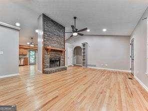 unfurnished living room with hardwood / wood-style floors, a stone fireplace, and ceiling fan