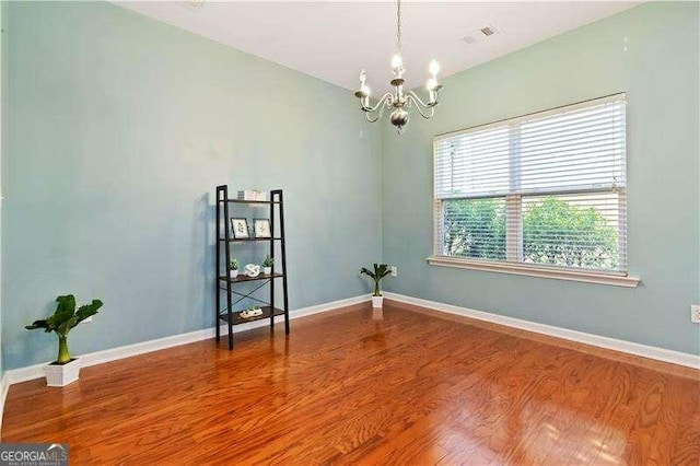 empty room featuring wood-type flooring and a notable chandelier