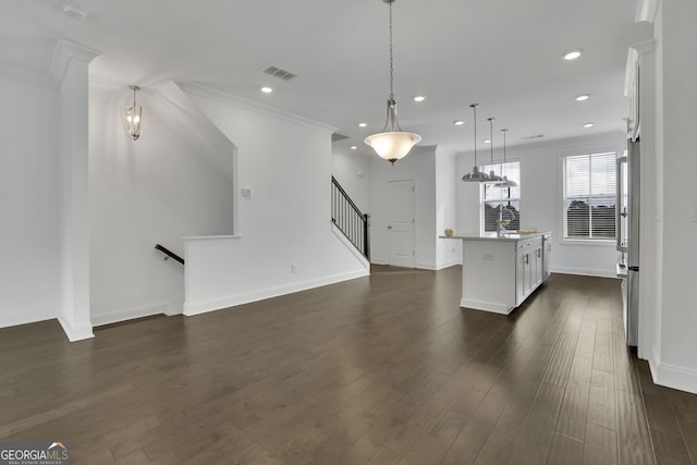 kitchen featuring ornamental molding, dark hardwood / wood-style floors, pendant lighting, a kitchen island with sink, and white cabinets