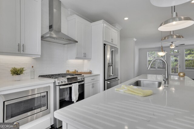 kitchen featuring sink, white cabinets, hanging light fixtures, stainless steel appliances, and wall chimney exhaust hood