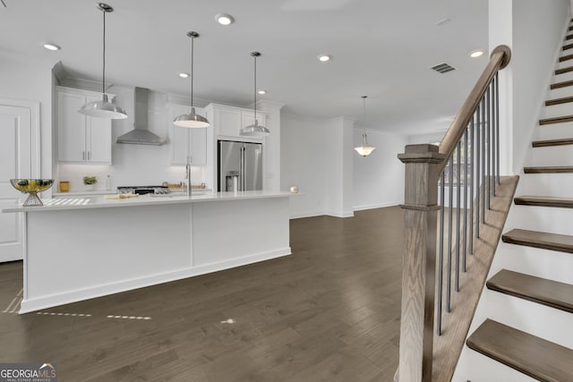 kitchen with high end fridge, a large island with sink, pendant lighting, wall chimney range hood, and white cabinets