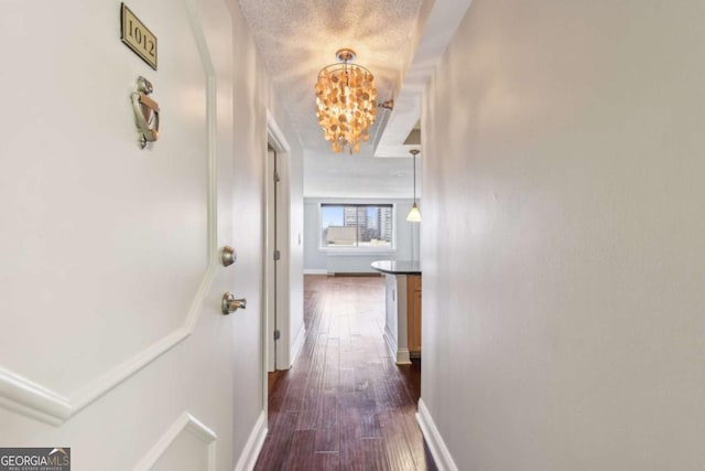 corridor with dark wood-style flooring, a textured ceiling, baseboards, and an inviting chandelier