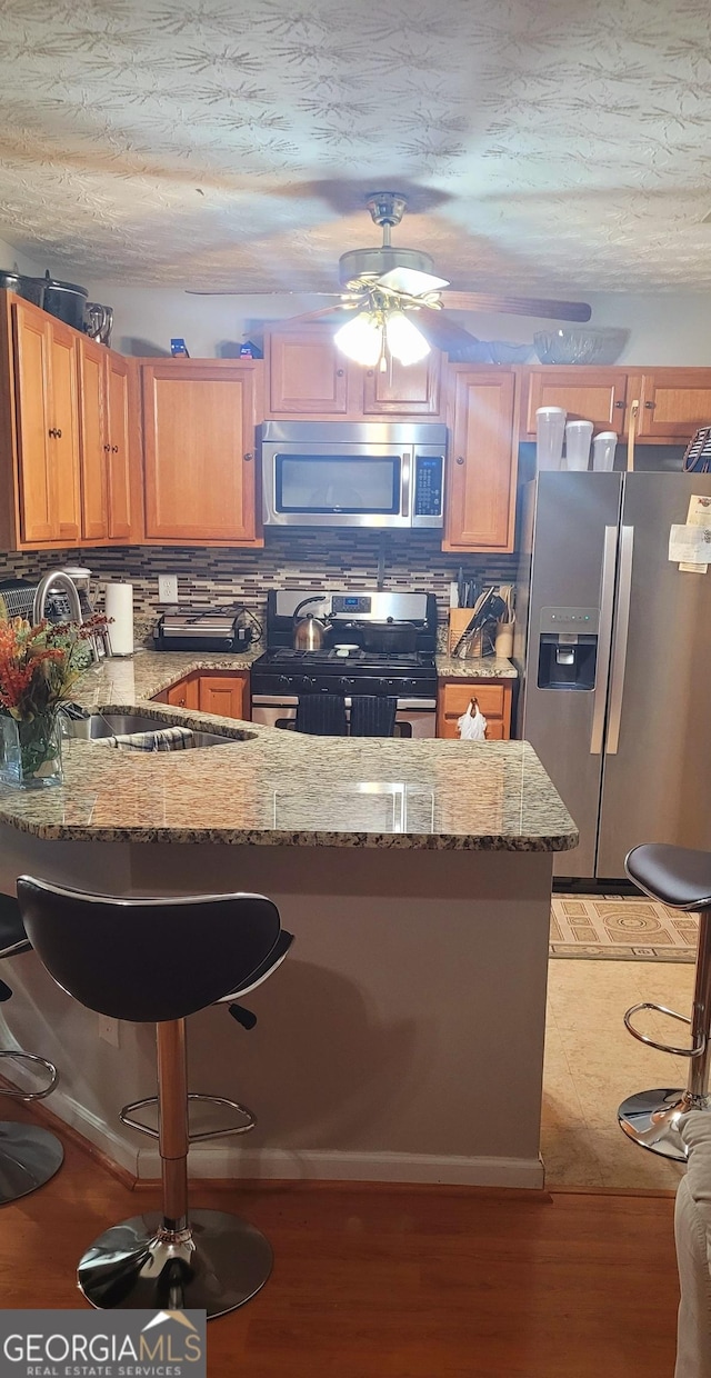 kitchen with tasteful backsplash, kitchen peninsula, stainless steel appliances, light stone countertops, and light hardwood / wood-style floors