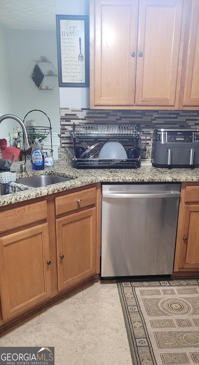 kitchen with tasteful backsplash, stainless steel dishwasher, sink, and light stone counters