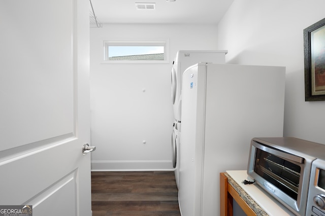 laundry area featuring stacked washer / drying machine and dark wood-type flooring