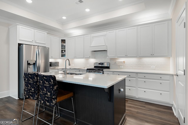 kitchen with sink, custom exhaust hood, a center island with sink, stainless steel appliances, and white cabinets