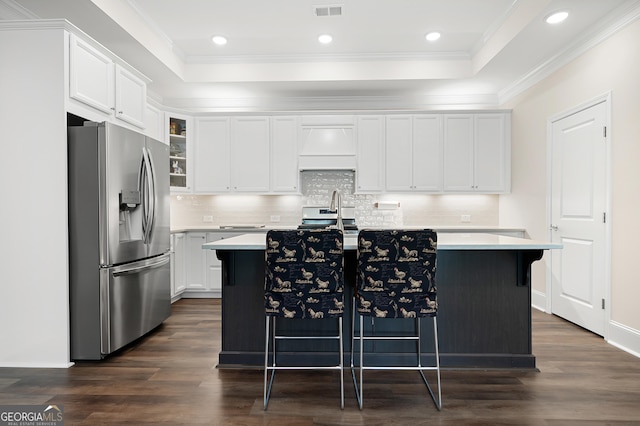 kitchen with white cabinetry, a center island with sink, stainless steel fridge, and a kitchen breakfast bar