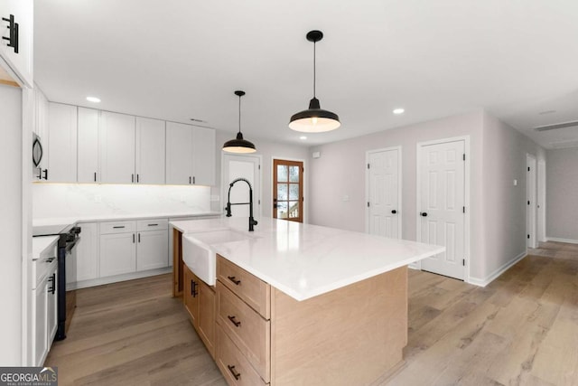 kitchen with sink, white cabinetry, hanging light fixtures, a center island with sink, and black / electric stove