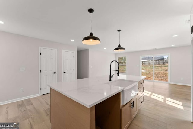 kitchen with pendant lighting, sink, a kitchen island with sink, light stone countertops, and light wood-type flooring