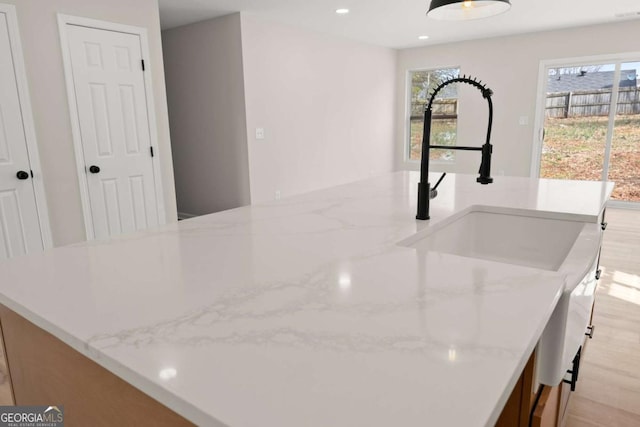 interior details featuring an island with sink, light stone countertops, sink, and light wood-type flooring