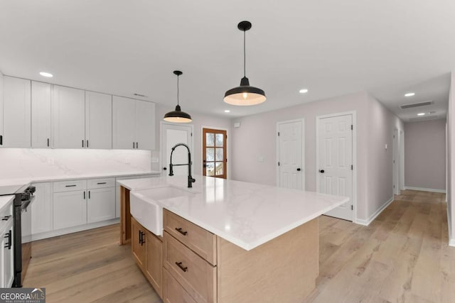 kitchen featuring pendant lighting, sink, white cabinetry, stove, and an island with sink