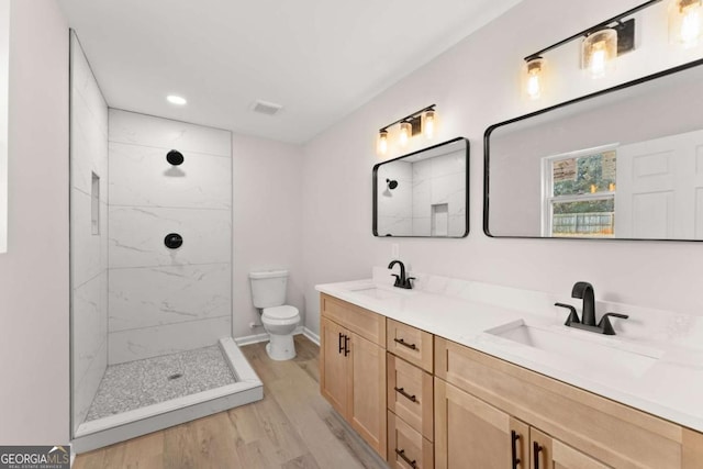 bathroom with a tile shower, hardwood / wood-style floors, vanity, and toilet