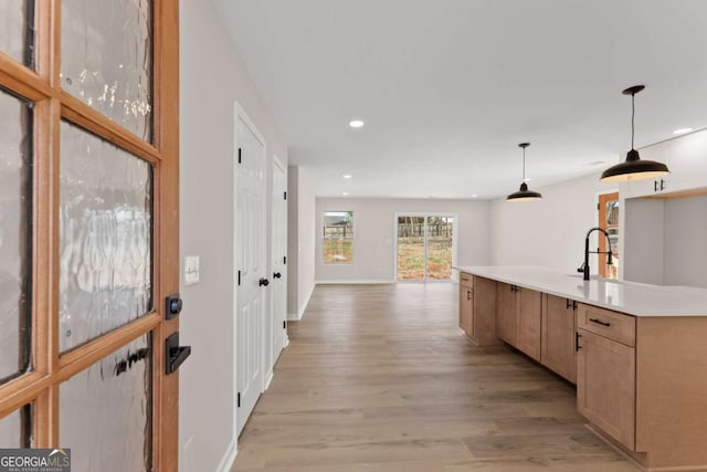 kitchen featuring light brown cabinetry, sink, decorative light fixtures, a center island with sink, and light hardwood / wood-style floors