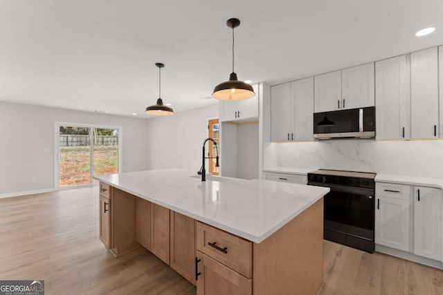 kitchen featuring sink, electric range, pendant lighting, a kitchen island with sink, and white cabinets