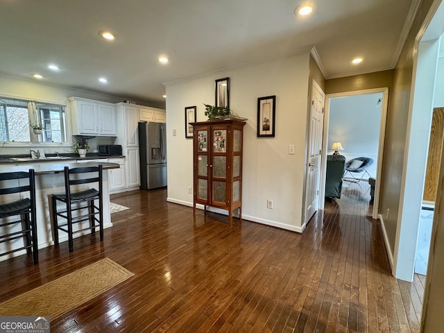 kitchen featuring stainless steel refrigerator with ice dispenser, dark wood-type flooring, a breakfast bar area, white cabinetry, and ornamental molding