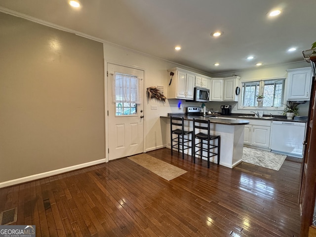 kitchen featuring dishwasher, white cabinets, a kitchen bar, ornamental molding, and kitchen peninsula