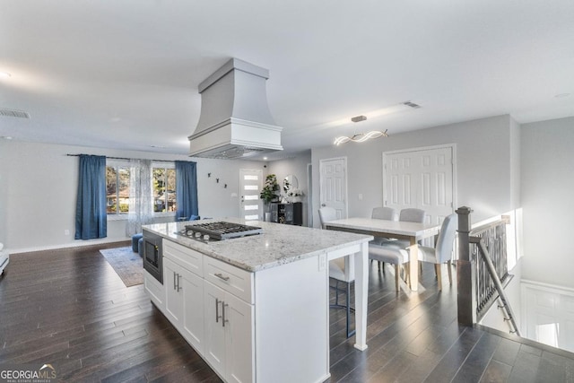 kitchen featuring built in microwave, stainless steel gas cooktop, custom exhaust hood, a kitchen island, and white cabinets