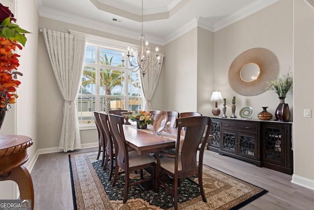 dining space with an inviting chandelier, a tray ceiling, crown molding, and hardwood / wood-style floors