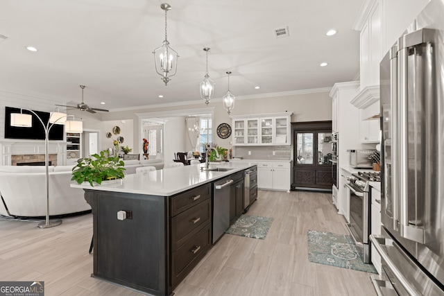 kitchen featuring sink, appliances with stainless steel finishes, an island with sink, white cabinets, and decorative light fixtures