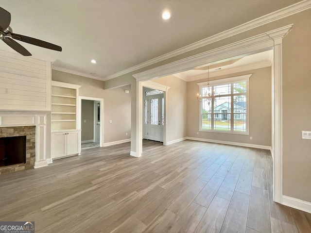 unfurnished living room with ornamental molding, a stone fireplace, ceiling fan with notable chandelier, and light wood-type flooring