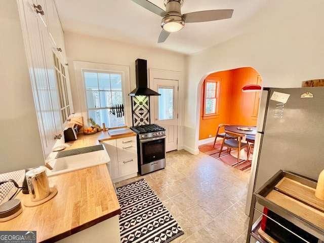 kitchen featuring white cabinetry, appliances with stainless steel finishes, wall chimney range hood, and ceiling fan