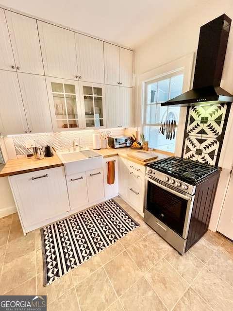 kitchen with stainless steel gas range, sink, exhaust hood, white cabinets, and backsplash