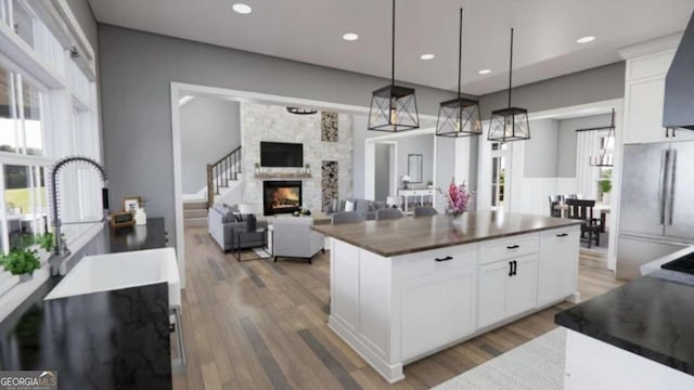 kitchen featuring dark wood-type flooring, a stone fireplace, white cabinetry, a center island, and pendant lighting