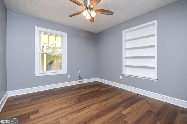 unfurnished room featuring ceiling fan, built in features, dark hardwood / wood-style floors, and a textured ceiling