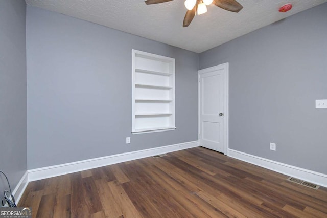 spare room with built in shelves, ceiling fan, dark wood-type flooring, and a textured ceiling