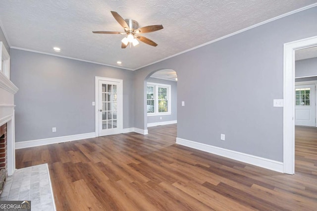 unfurnished living room featuring dark hardwood / wood-style flooring, ceiling fan, crown molding, a brick fireplace, and a textured ceiling