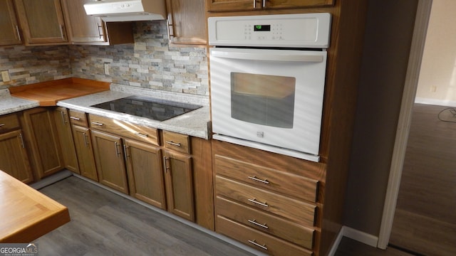 kitchen featuring black electric cooktop, decorative backsplash, light stone countertops, and white oven