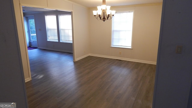 spare room with crown molding, a chandelier, a wealth of natural light, and dark hardwood / wood-style flooring