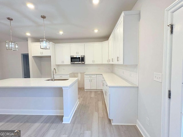 kitchen featuring a sink, white cabinetry, light wood-type flooring, decorative backsplash, and stainless steel microwave