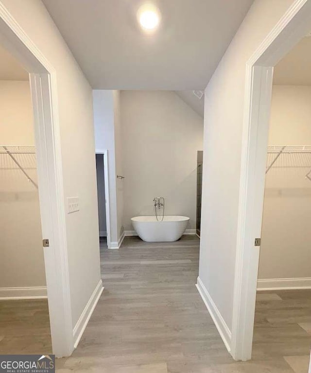 full bath featuring a spacious closet, a soaking tub, wood finished floors, and baseboards