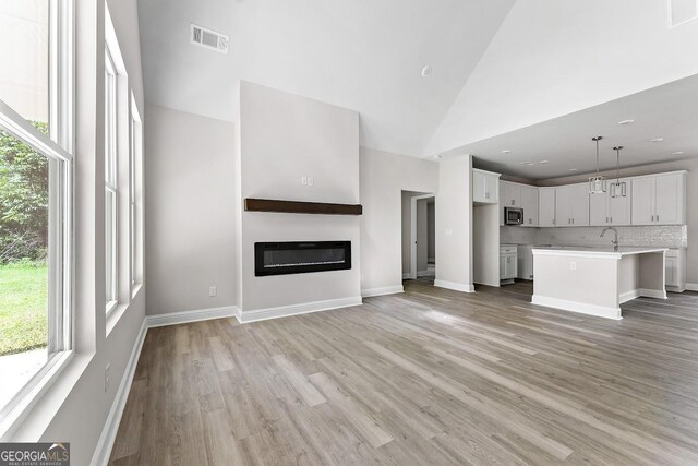 unfurnished living room with high vaulted ceiling and light hardwood / wood-style floors