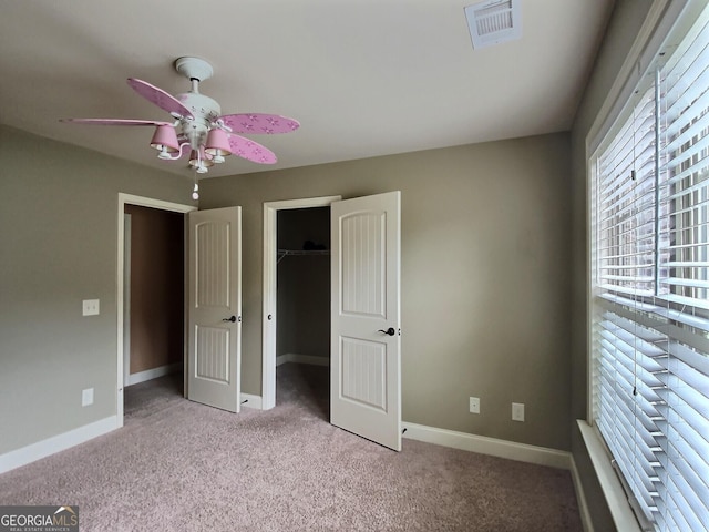 unfurnished bedroom featuring a walk in closet, light colored carpet, ceiling fan, and a closet