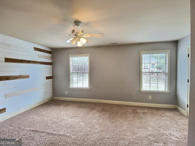 carpeted empty room with wooden walls and ceiling fan