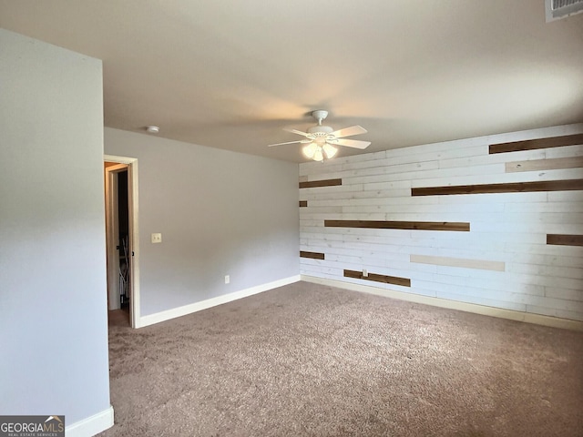 carpeted spare room with ceiling fan and wood walls