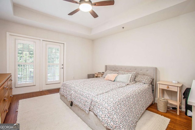 bedroom featuring a raised ceiling, dark hardwood / wood-style floors, access to outside, and ceiling fan