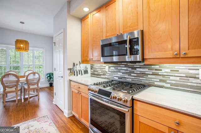 kitchen with decorative light fixtures, appliances with stainless steel finishes, hardwood / wood-style flooring, light stone countertops, and backsplash