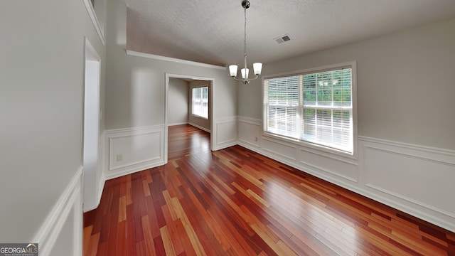 empty room featuring dark wood-type flooring, a chandelier, and a textured ceiling