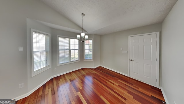 unfurnished dining area with hardwood / wood-style flooring, vaulted ceiling, a textured ceiling, and a chandelier