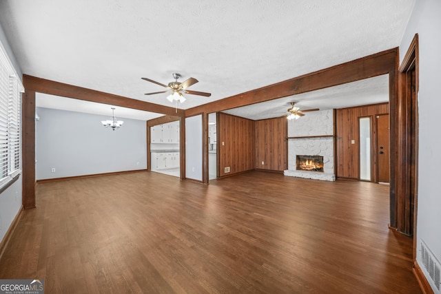 unfurnished living room featuring dark wood-type flooring, a fireplace, a textured ceiling, and wood walls