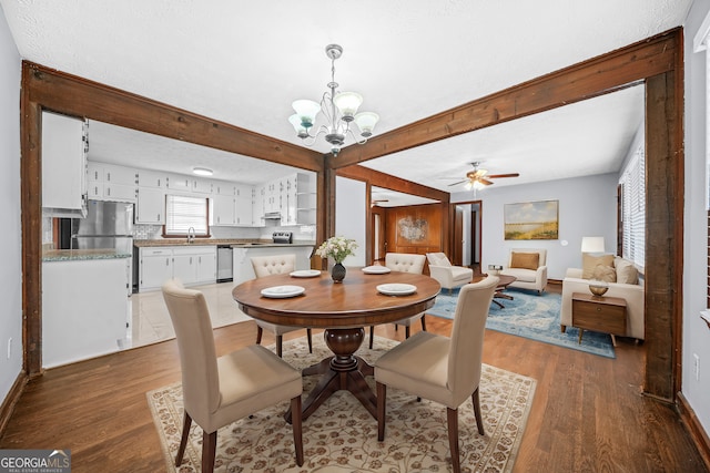 dining space with sink, beam ceiling, dark wood-type flooring, and ceiling fan with notable chandelier