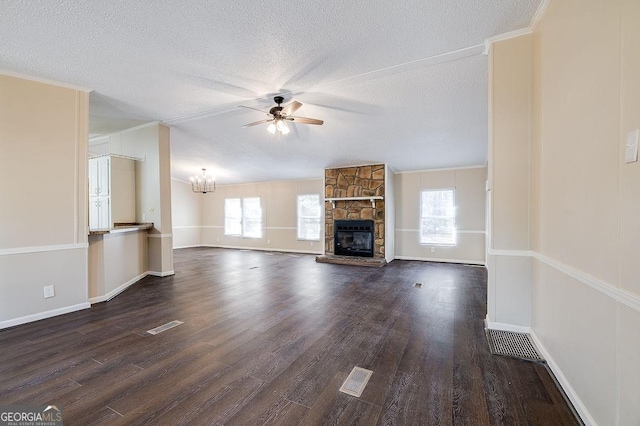 unfurnished living room with a stone fireplace, ceiling fan with notable chandelier, ornamental molding, dark wood-type flooring, and a textured ceiling