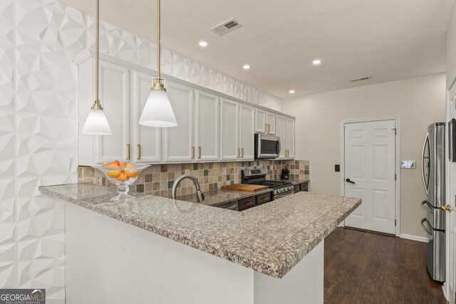 kitchen featuring appliances with stainless steel finishes, white cabinetry, light stone countertops, decorative light fixtures, and kitchen peninsula