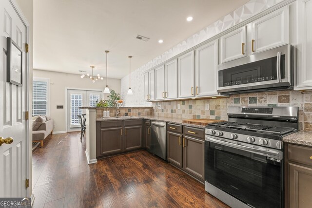 kitchen featuring appliances with stainless steel finishes, decorative light fixtures, backsplash, kitchen peninsula, and light stone countertops