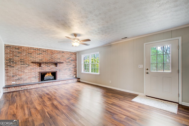 unfurnished living room featuring hardwood / wood-style floors, crown molding, a fireplace, and a textured ceiling