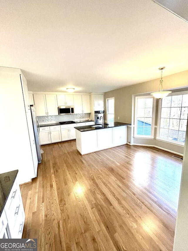 kitchen featuring tasteful backsplash, hanging light fixtures, light wood-type flooring, appliances with stainless steel finishes, and white cabinets